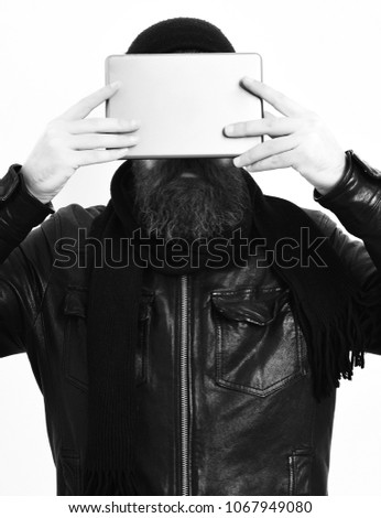 Bearded man, long beard. Brutal caucasian serious unshaven hipster holding tablet in black leather jacket, hat and scarf isolated on white studio background