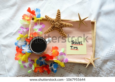 A wooden tray with summer decorations  and a note with travel tips text on a white sheet with a cup of coffee