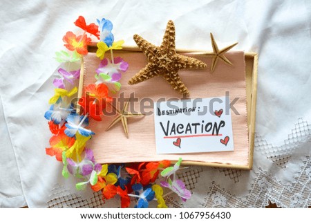 A wooden tray with summer decorations  and a note with destination vacation text on a white sheet 