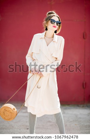 Lifestyle portrait of a pretty woman dressed in pink coat standing on the dark red wall background outdoors