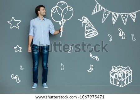 Amazing party. Cheerful young handsome man coming to a nice Birthday party and smiling while holding balloons