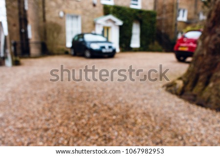 Blurred image of a driveway next to a house with parked cars.