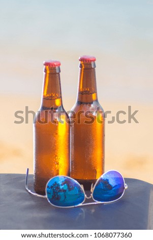Brown beer bottles and blue sunglasses on a table on the background of the sea and sky