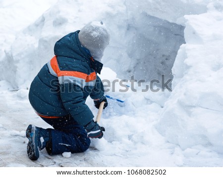 European boy is digging a snow cave in the yard.