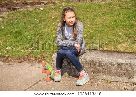 Teenage girl sad sitting on the grass with a skate.