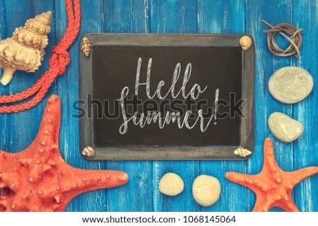Blackboard with "Hello Summer" chalk text, with sea shells, rope and star fish on blue  wooden background