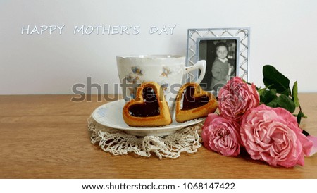 A picture of a 1969 vintage with little girl, next to a cup of coffee and a heart-shaped cookie and pink roses on a wooden table.
Mother's day background.