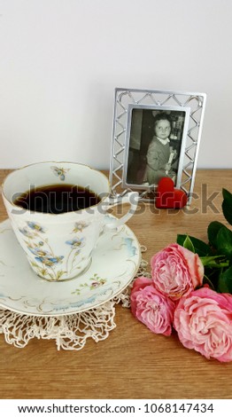 A picture of a 1969 vintage with little girl, next to a cup of coffee and a heart-shaped cookie and pink roses on a wooden table.
Mother's day background.