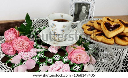 A picture of a 1969 vintage  withlittle girl, next to a cup of coffee and a heart-shaped cookie and pink roses on a tray with a crochet napkin.
