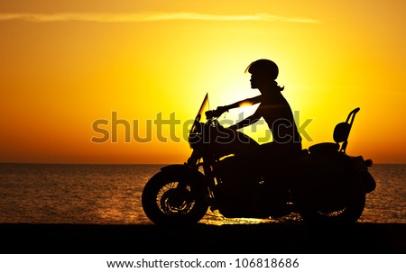 Woman biker over sunset, female riding motorcycle, motorbike driver traveling, girl racing on the beach road, freedom lifestyle Royalty-Free Stock Photo #106818686