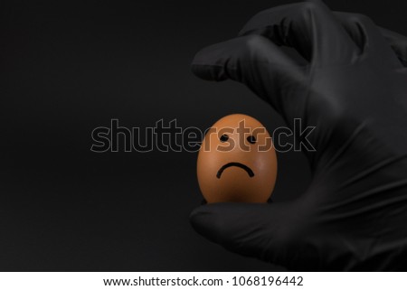 funny eggs with faces, on black background, hand in a black glove holding an egg