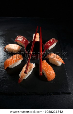 Presentation of a circular shaped sushi plate on a black slate background with chopsticks