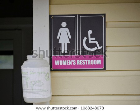 Sign outside a women's restroom, with a white jar for placing mounted on the wall