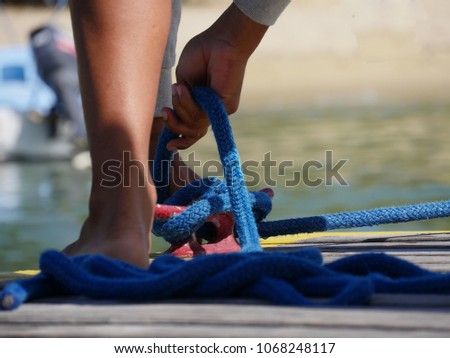 Picture of hands tying a blue braided rope to secure a boat to the pier