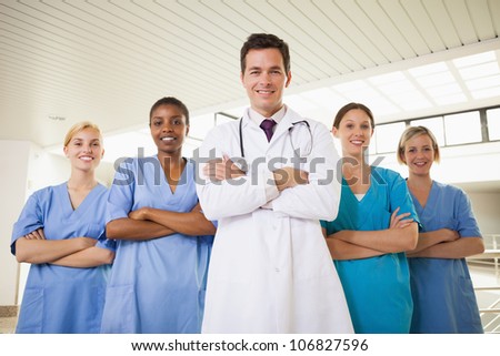 Smiling doctor and nurses with arms crossed in hospital corridor