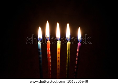 Cake candles on a dark background stock images. Colored cake candles. Burning cake candles. Birthday background images. Party candles on a black background