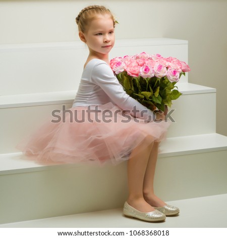 A cute little girl with a bouquet of flowers sits on a white staircase. The concept of happy people, childhood.