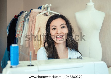 portrait of a beautiful seamstress brunette with long hair working with a sewing machine. tailor creates a collection of outfits . young female fashion designer sewing a dress