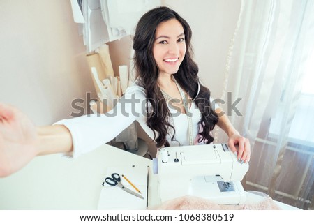 beautiful woman seamstress with long hair does selfie. tailor creates a collection of clothes on the background of a sewing machine. concept of online sewing education