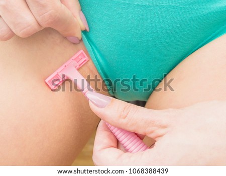 Young caucasian woman with a pink razor shaving her bikini area, part of body, close up. 