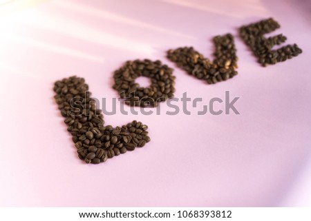 Spilled roasted coffee beans on a pink background with a love inscription.
