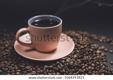 Cup of black steaming coffee on a spilled roasted coffee beans on a black background.