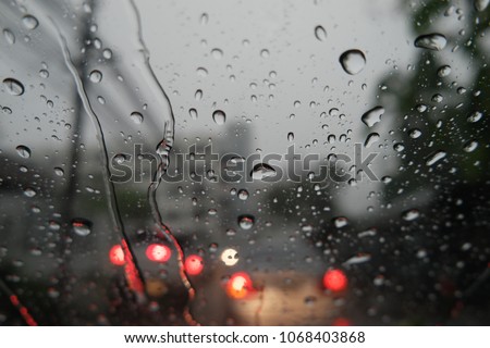 Blur image, water drops on the windshield, traffic in the city on a rainy day, car windshield view, colorful bokeh, dark background.