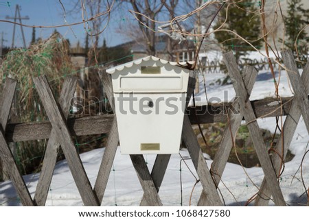 The damaged mailbox, in the form of a house, hangs on a wooden fence in the spring.