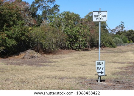 black and white No Through Road and One Way with arrow traffic signs on a metal pole