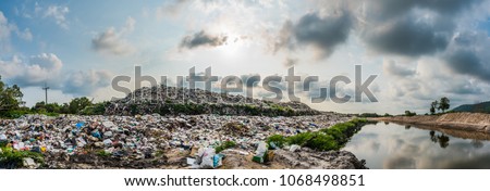 The panorama of large heap garbage dump extends parallel to the river,Garbage mountains with cloudy sky  back ground in day light,Waste has petroleum products are the major. Royalty-Free Stock Photo #1068498851