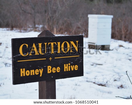 Wooden Caution Honey Bee Hive Sign, with bee box in background during winter