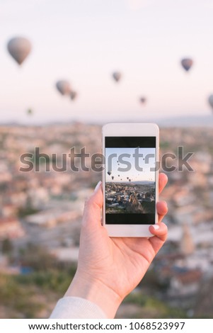Smartphone in woman's hands, tourist girl taking photo on beautiful landscape and balloons in Cappadocia with mobile camera, sunrise time, dreamy travel concept