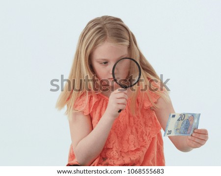 Girl holding a 20 euro banknote under a magnifying glass.