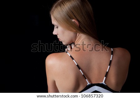Pretty Caucasian woman with long blond hair before a black background with her back to the camera and looking over her left shoulder