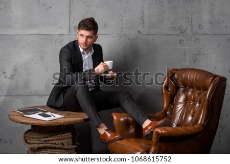 Portrait of young businessman project manager sitting in a chair on grey background loft cabinet interior copy text