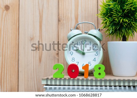 2018 letters text and notebook paper, alarm clock and little decoration tree in white vase on wooden background, working for year 2018 concept idea.