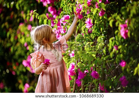 Beautiful little girl in pink glamor dress with pigtails and smiling face in spring pink flower blooming sunny day