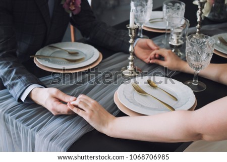 Closeup of couple hands on restaurant table with two glasses of champagne. Romantic couple holding each other's hand at dinner in a luxury restaurant.