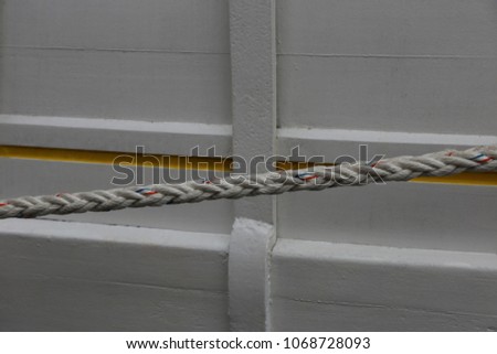 Close up outdoor view of part of a white ancient wooden boat. Large oblique rope in front of the hull made of planks. Yellow decorative painted line. Abstract picture of the detail of on old vessel.