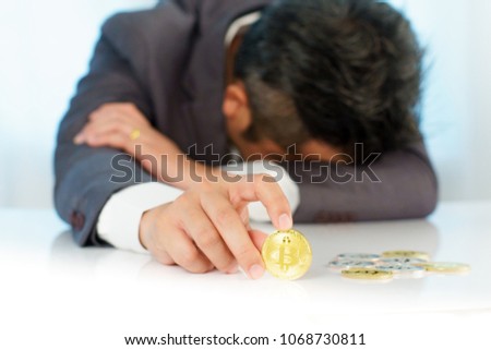 Sad business man in suit looking at golden Bitcoin , a digital symbol of virtual currency in his finger play on white table.
