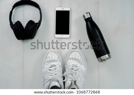 Black a headphones and white smartphone with sports sneakers shoes, bottle of water on a woodenbackground, top view, flat lay photo Royalty-Free Stock Photo #1068772868