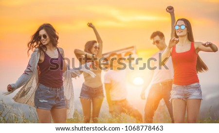 The young people with a boom box dancing in the background of the sunset