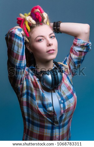 Beautiful young girl with colored narrated dreadlocks in headphones on the neck. Isolated on a blue background.