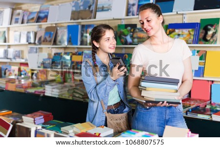 Girl is choosing book while chatting in bookstore. 