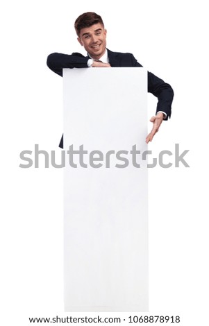 excited businessman presenting while resting an elbow on white billboard. He is standing on a white background behind it, full body picture.