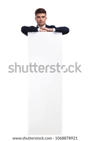 businessman resting elbows on a big white empty board while standing on white background behind it, full body picture.