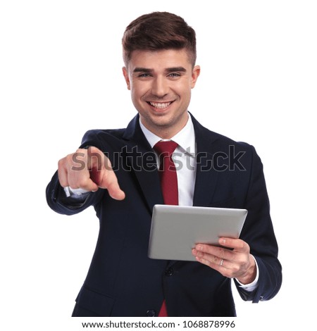 portrait of excited businessman holding grey tablet and pointing finger on white background. he wears a navy suit and a red tie.