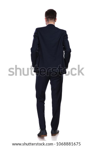 back view of businessman standing with hands in pockets on white background while wearing a navy suit, full body picture