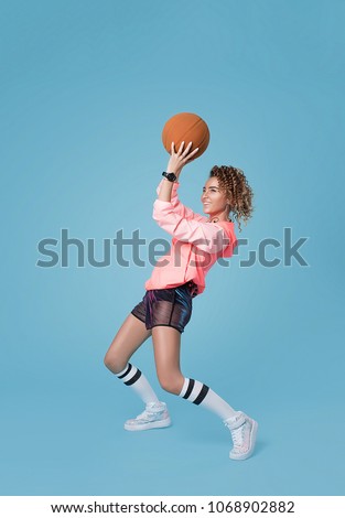 A young beautiful girl in a bright sports jacket and shorts with a trendy and stylish hairstyle holds a basketball in her hands and wants to throw it into the basket Royalty-Free Stock Photo #1068902882
