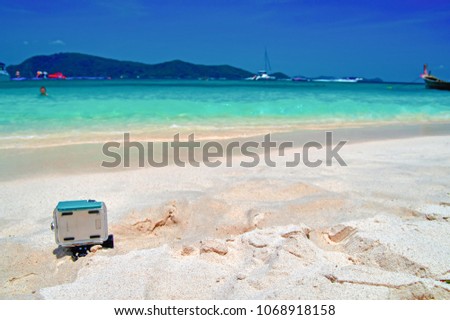 Seascape. Action camera in a protective box stands on the sand on tropical beach. Rear view. Copy space. Turquoise water, blue sky, white sand.